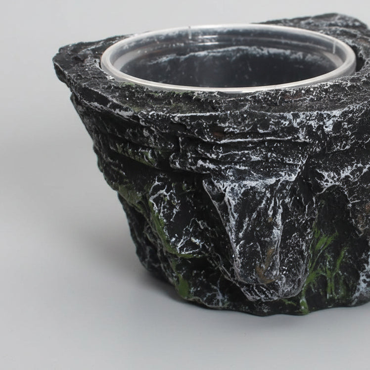 A close-up of a black and gray rock-textured planter pot with a circular opening, shown against a plain white background.