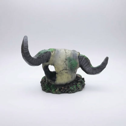 A decorative horned animal skull sculpture, resembling a bison or wild ox skull, with textured dark gray horns and green mossy details, set against a plain white background.