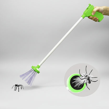 A handheld long-handled bug and spider trap with a bright green handle, white shaft, and purple sticky brushes at the tip. A hand is holding the top, and a small spider is shown near the trap, with a circular inset demonstrating the trapping effect.