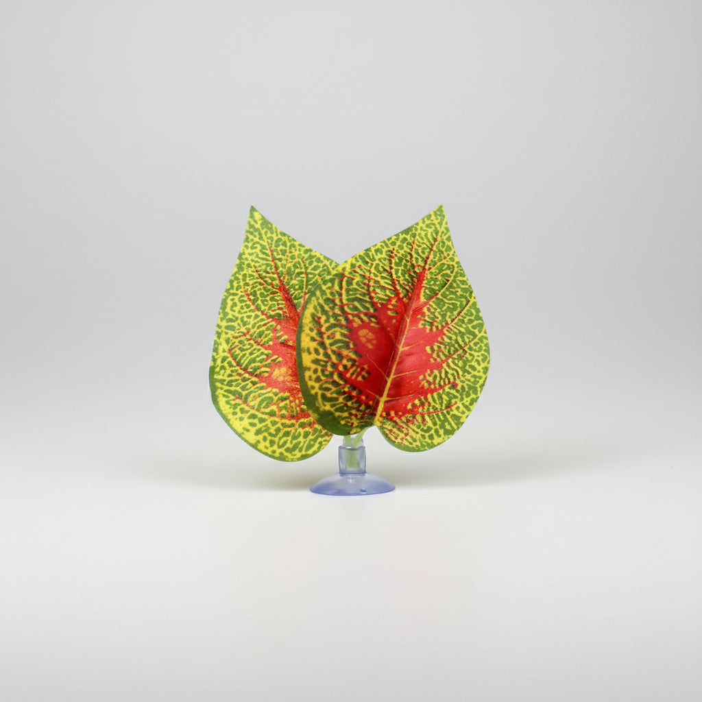 Three artificial decorative leaves with green, yellow, and red variegated patterns on a clear stand, shown on a white background with the brand name NOMOY PET in the top left corner.